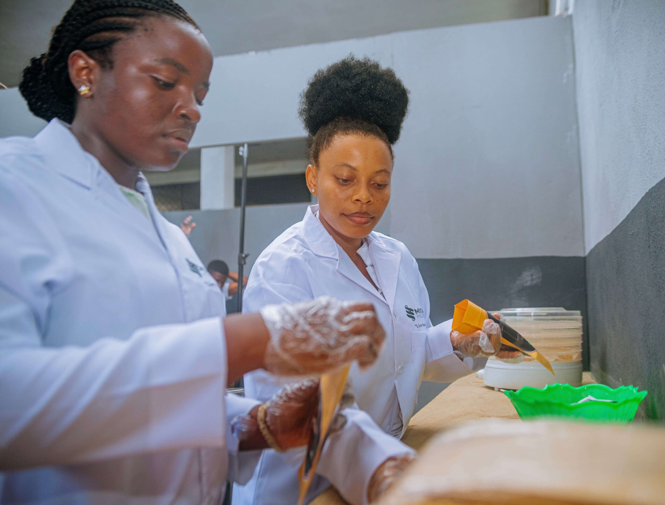 Two Mumita staff in lab coats and gloves fill kraft pouches of dried vegetables