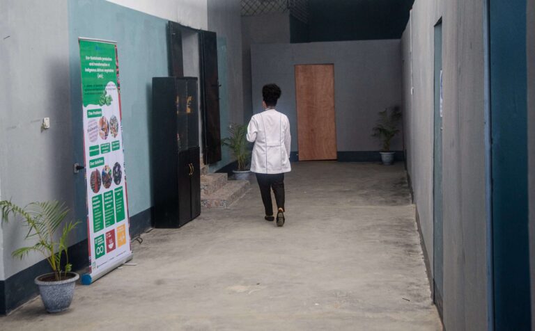 A staff member in a white coat walks down a corridor of the Bonduma Gate facility, past a pull-up banner