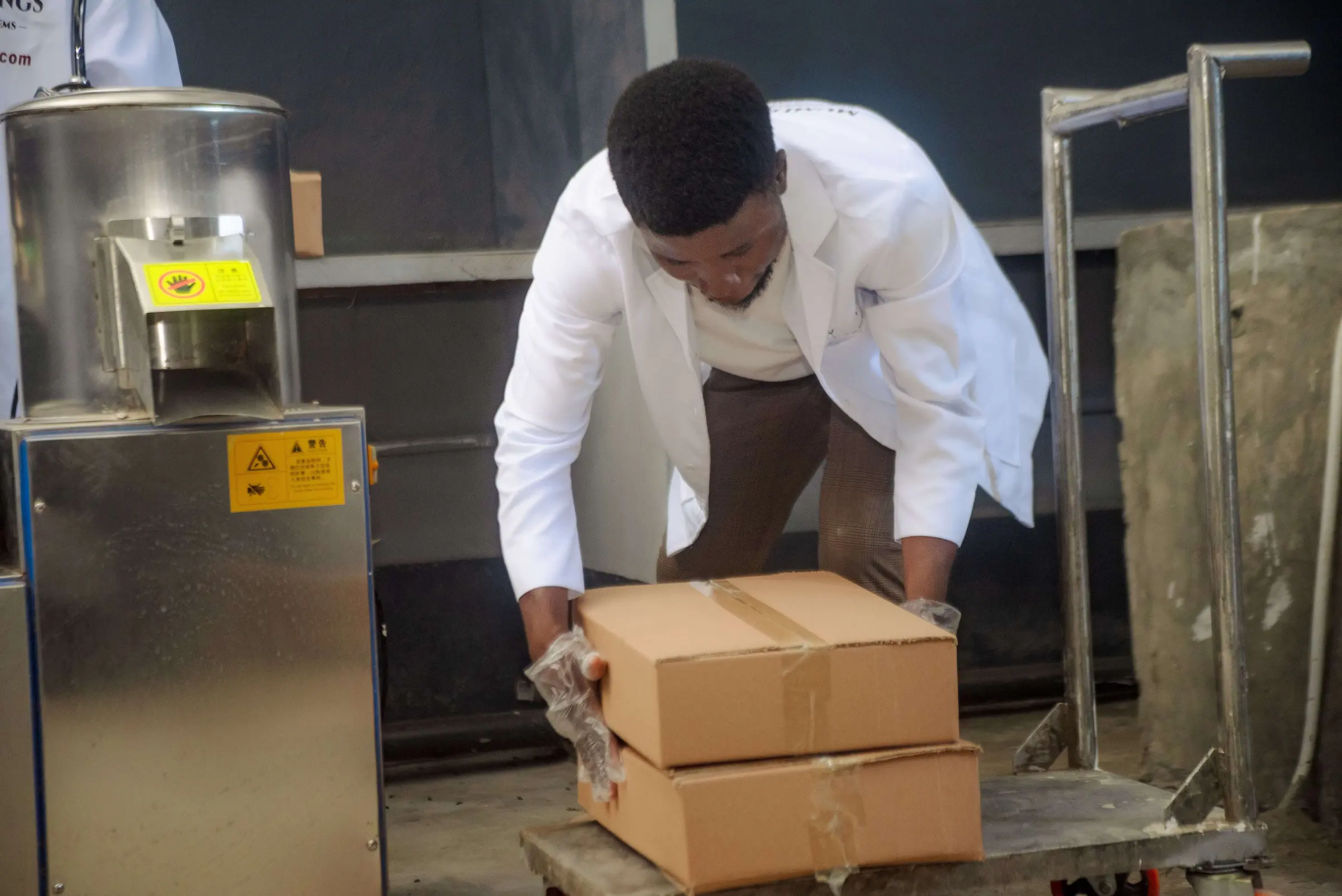 A Mumita staff member in a white coat lifts cartons onto a trolley