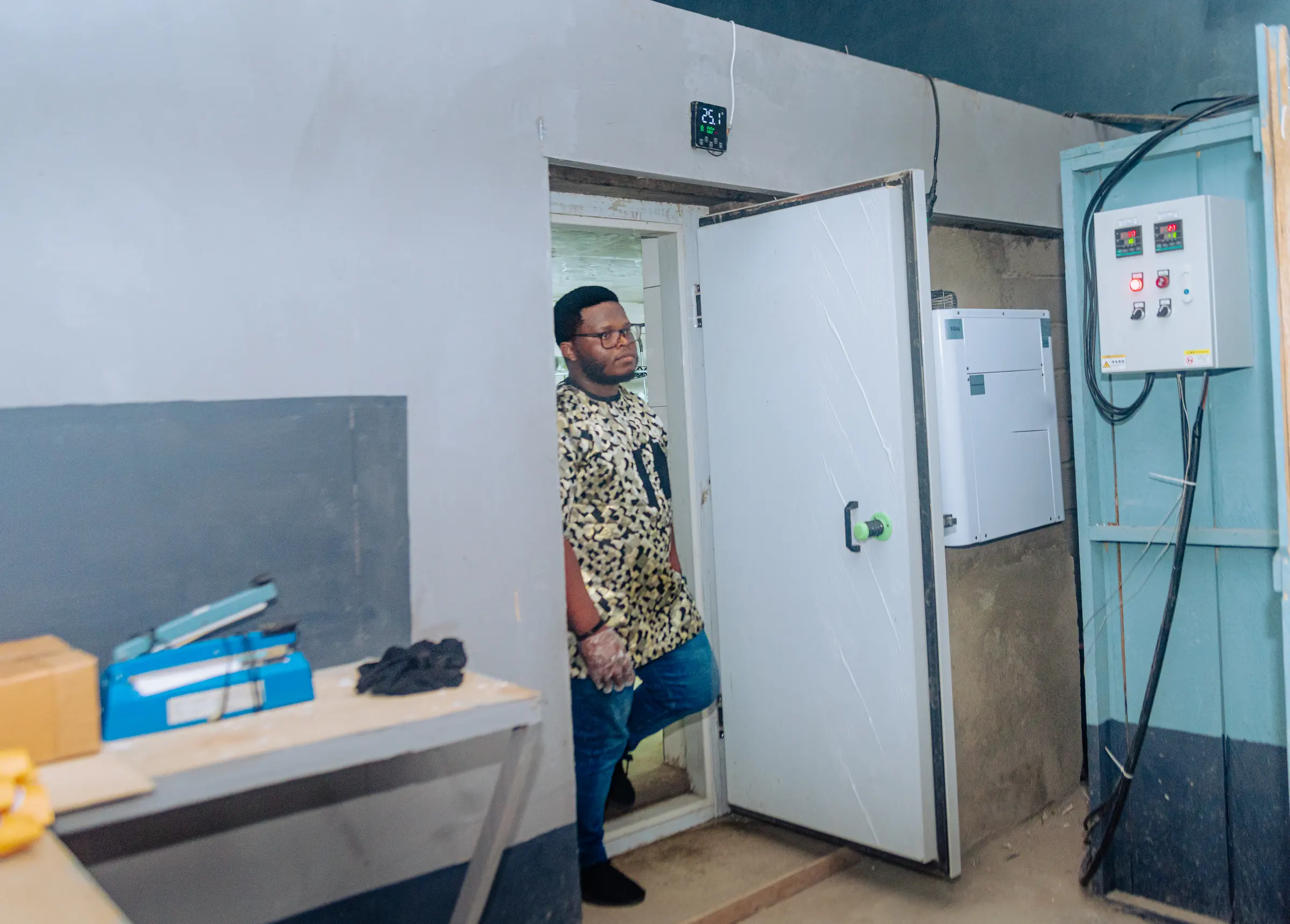 A staff member steps out of the cold room beside its temperature control panel