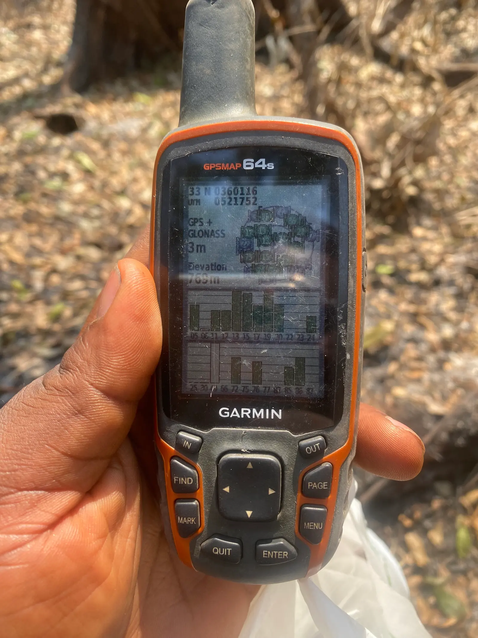 A hand holds a Garmin GPS unit over a field during farm mapping