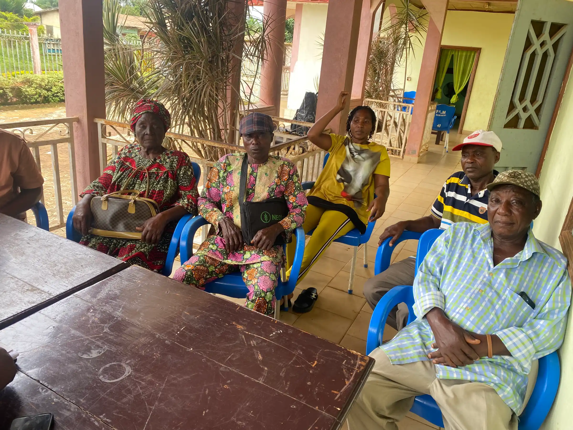 Older farmers seated in plastic chairs at a meeting on a veranda