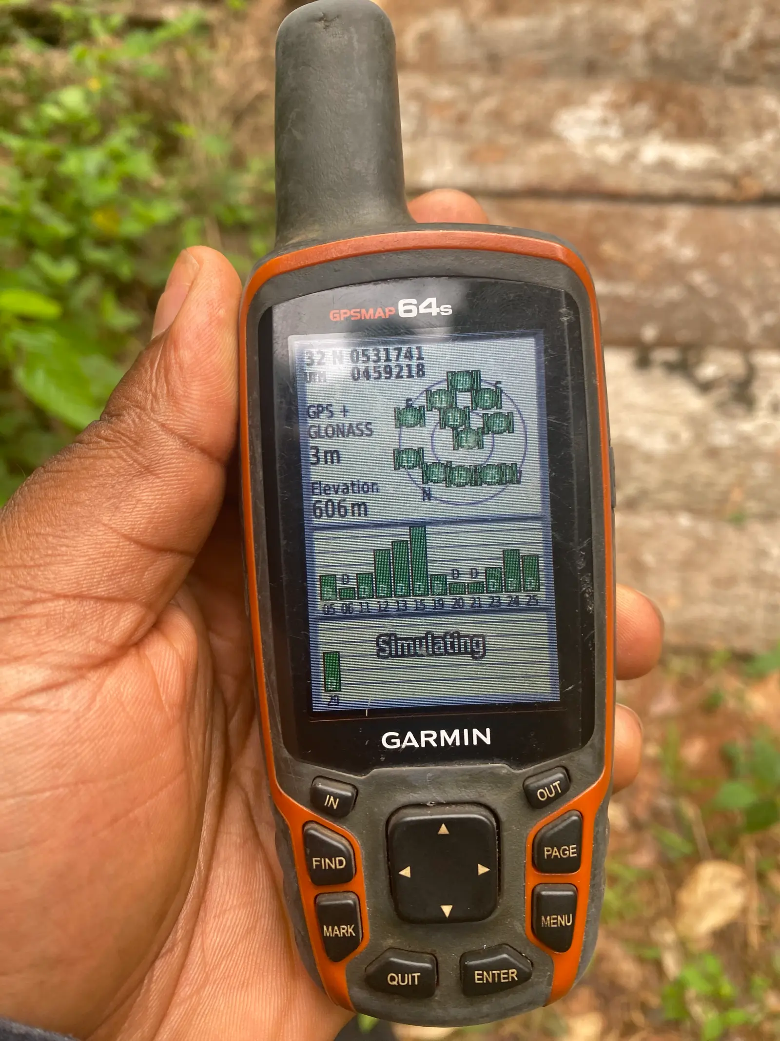 A hand holds a handheld GPS unit showing satellite readings