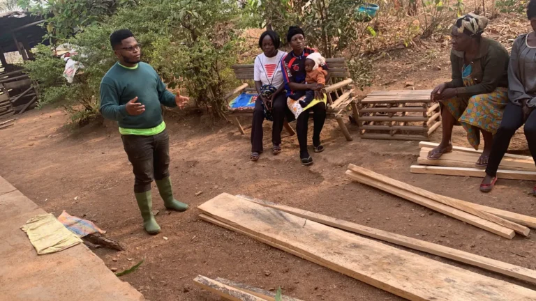 A trainer speaks to women beside stacked timber for raised beds