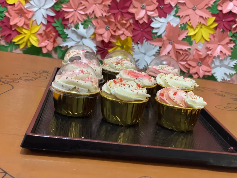 A tray of Praïs cupcakes before a paper-flower wall