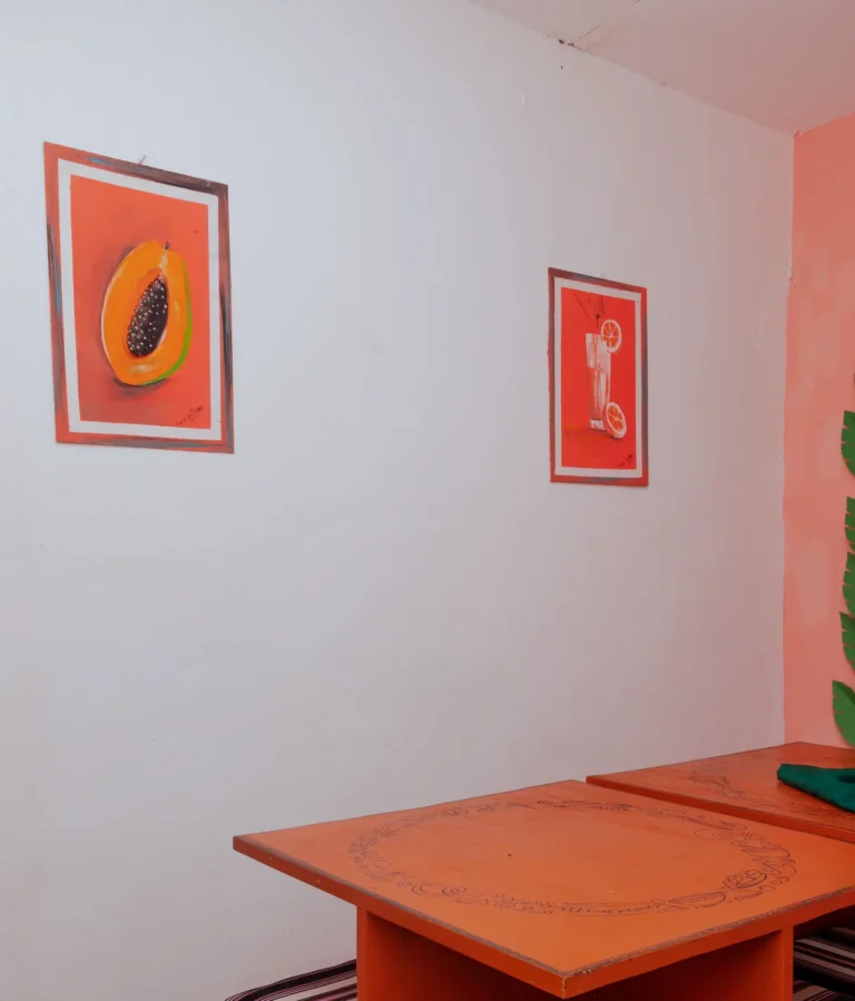 A corner of the Praïs dining room with orange tables and fruit paintings