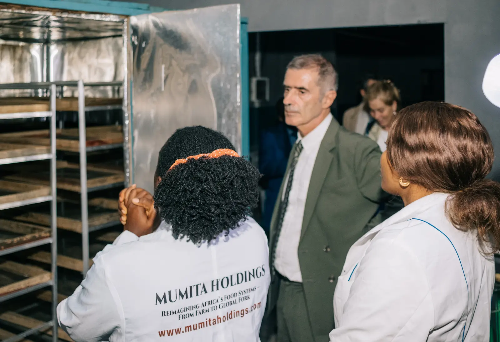 A staff member in a Mumita Holdings coat stands beside the drying cabinet with visitors
