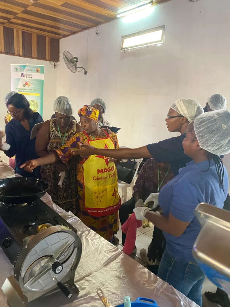 Trainees in hairnets work at a plantain slicer and frying station